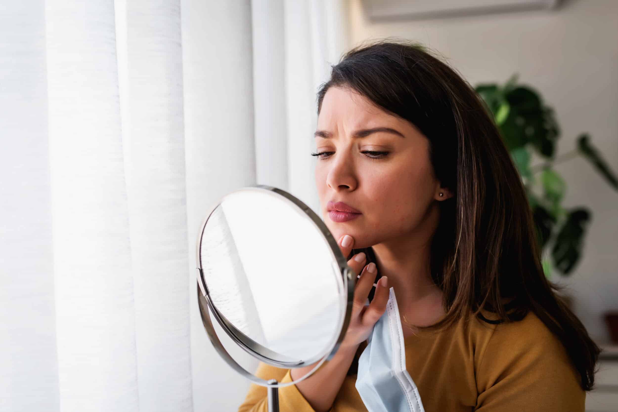 Woman examining her skin in the mirror needing VISIA Skin Analysis in East Greenwich